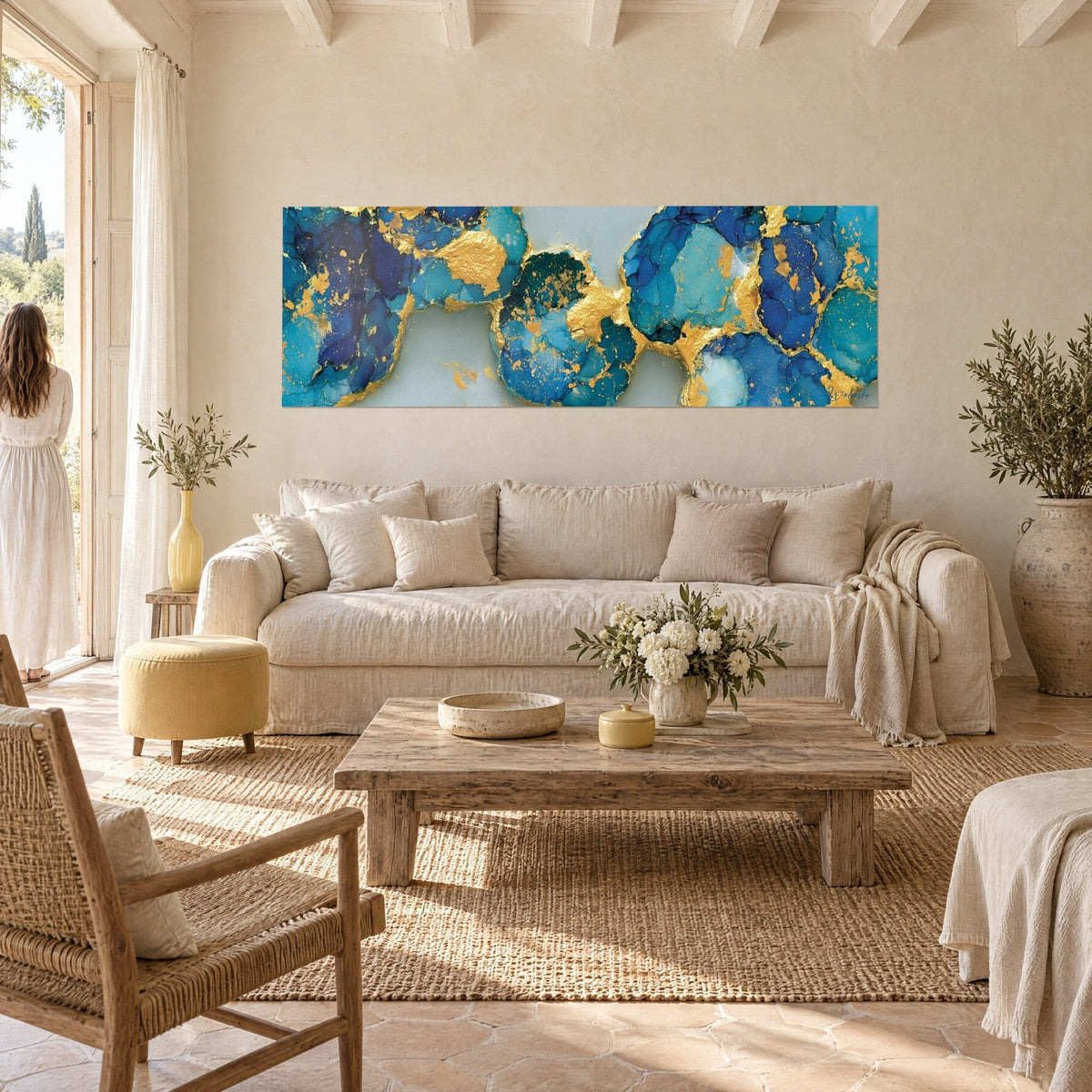 Tableau marbrures bleu nuit et turquoise veinées d'or, une femme de dos le regarde, au-dessus d'un canapé dans un salon lumineux