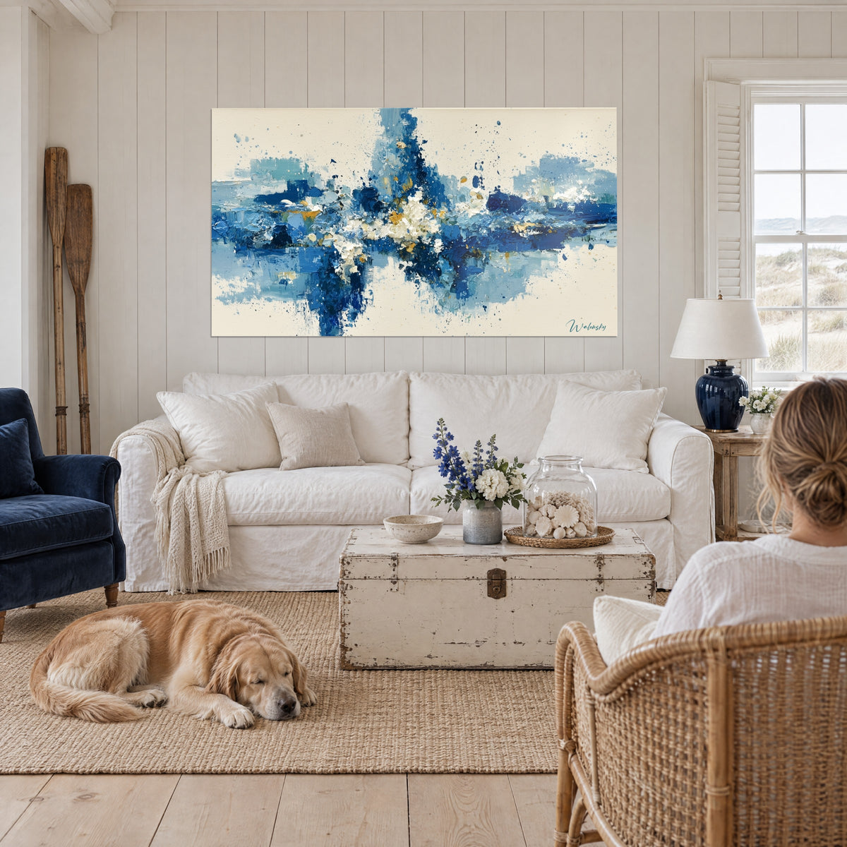 Tableau éclaboussure bleu marine et ivoire aux touches dorées, deux personnes de dos et un retriever, au-dessus d'un canapé dans un salon lumineux