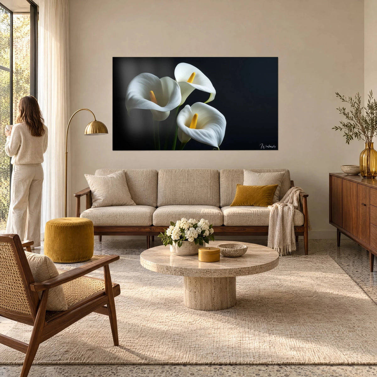 Tableau trois arums blancs à cœur jaune sur fond noir, femme de dos devant, au-dessus d'un canapé dans un salon lumineux