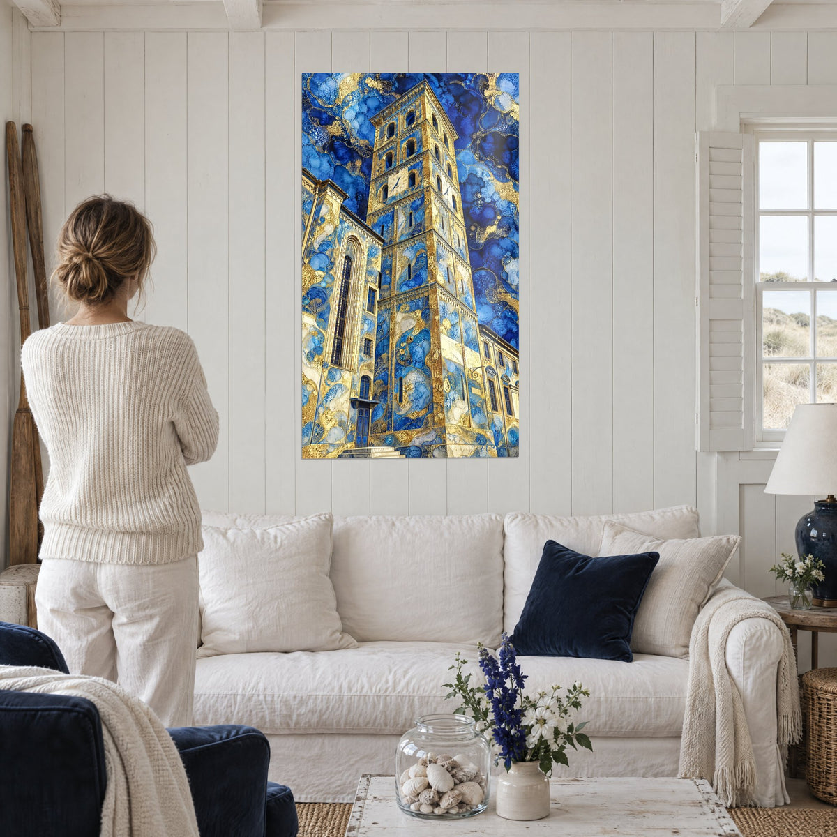 Tableau campanile de pierre ocre aux marbrures bleu marine et or, femme de dos, au-dessus d'un canapé dans un salon lumineux