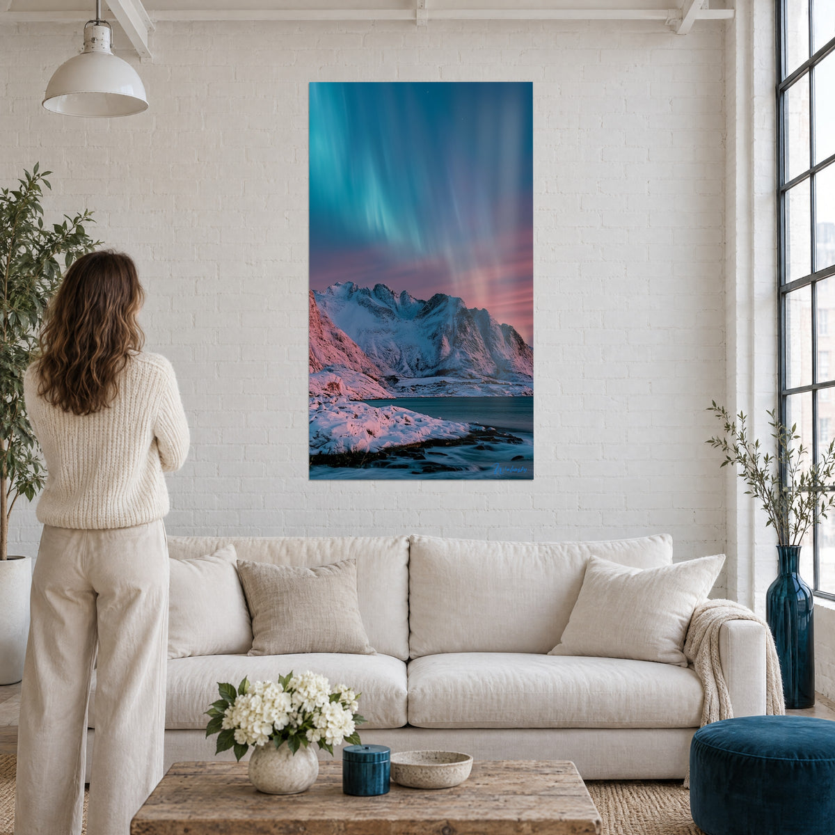 Wall art turquoise northern lights over pink snowy peaks, woman seen from behind, above a sofa in a bright living room
