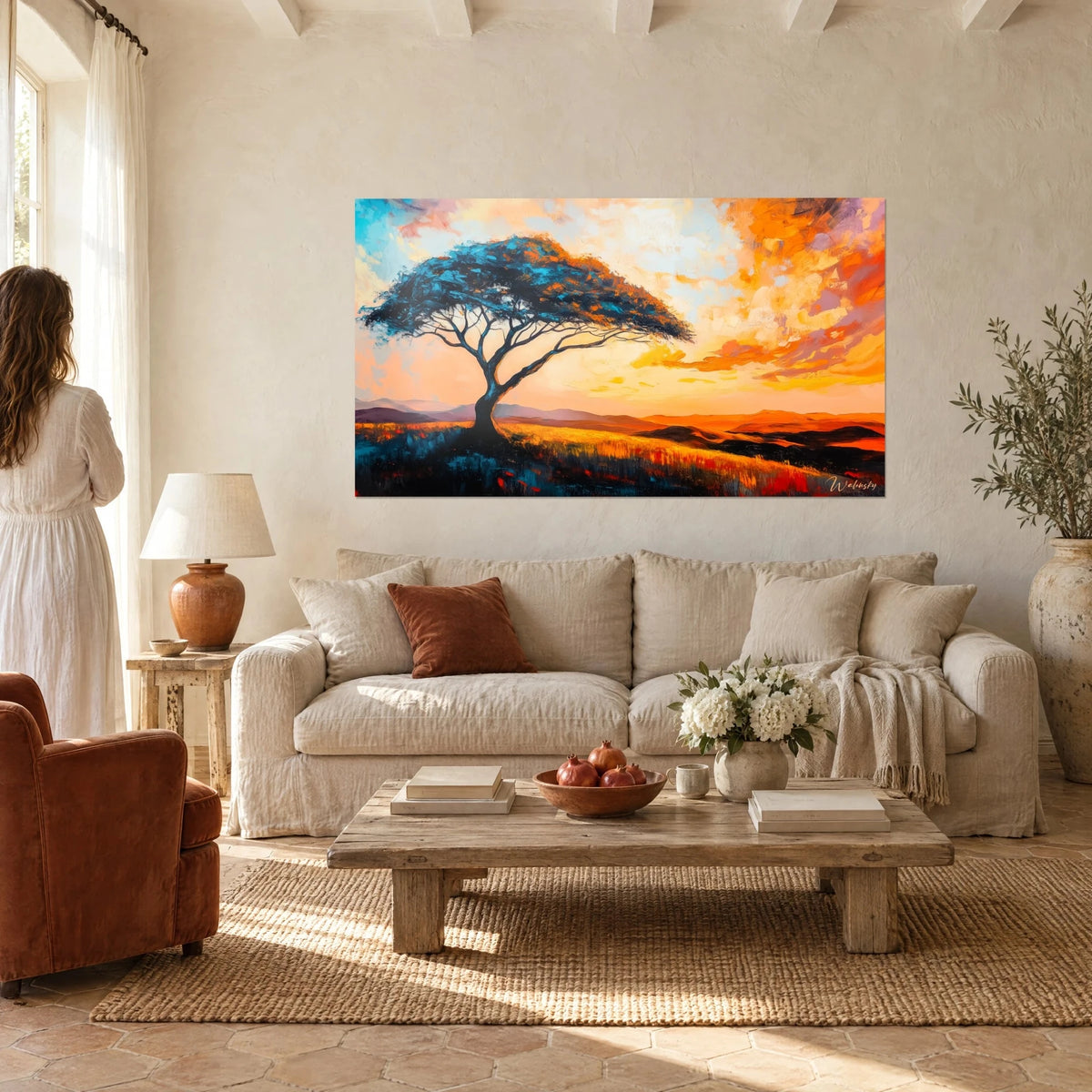 Tableau acacia parasol aux feuilles turquoise sous un ciel orange et rose, femme de dos, au-dessus d'un canapé dans un salon lumineux