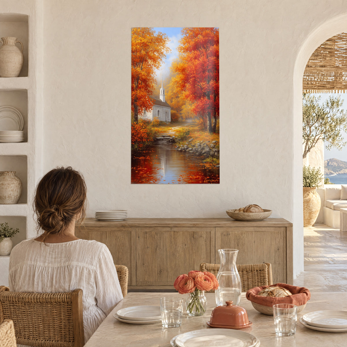 Wall art country church with carmine and honey-colored leaves, misty path, young woman seen from behind seated at a kitchen table with white arches