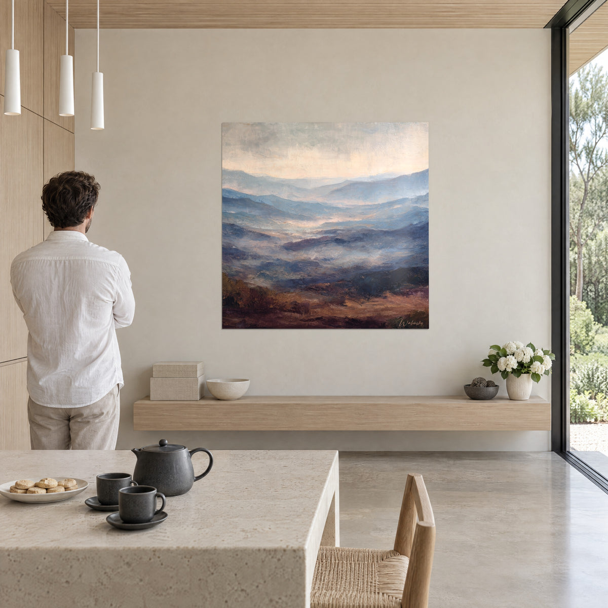 Wall art peaks softened by morning mist, slate blue and golden sand, man seen from behind, in a dining room