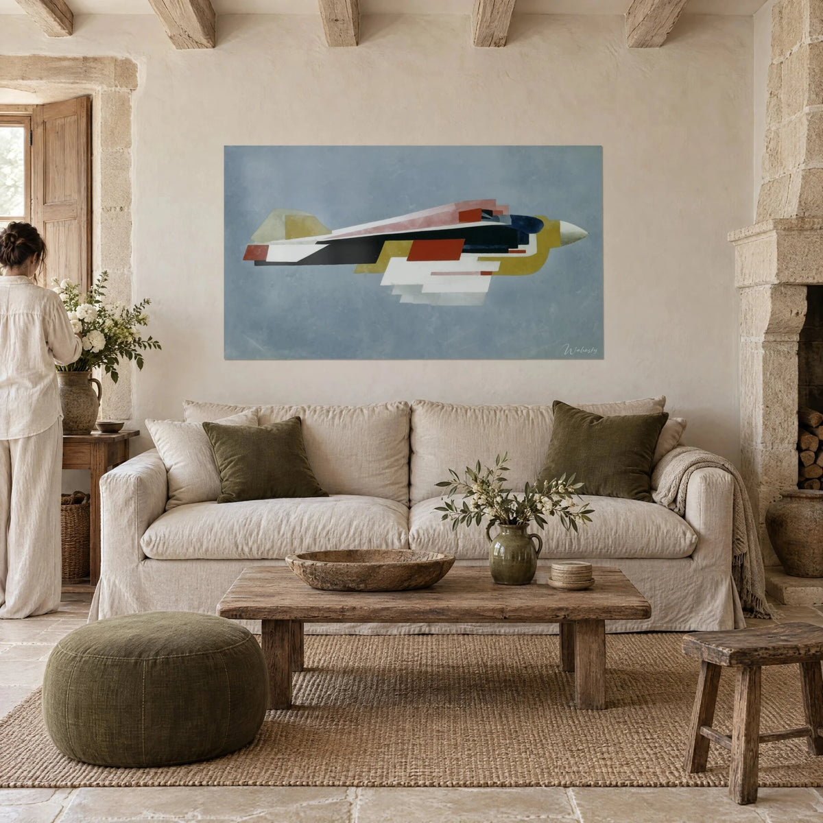 Wall art constructivist airplane with rust and ochre wings against a blue-grey sky, seen from behind, above a sofa in a bright living room
