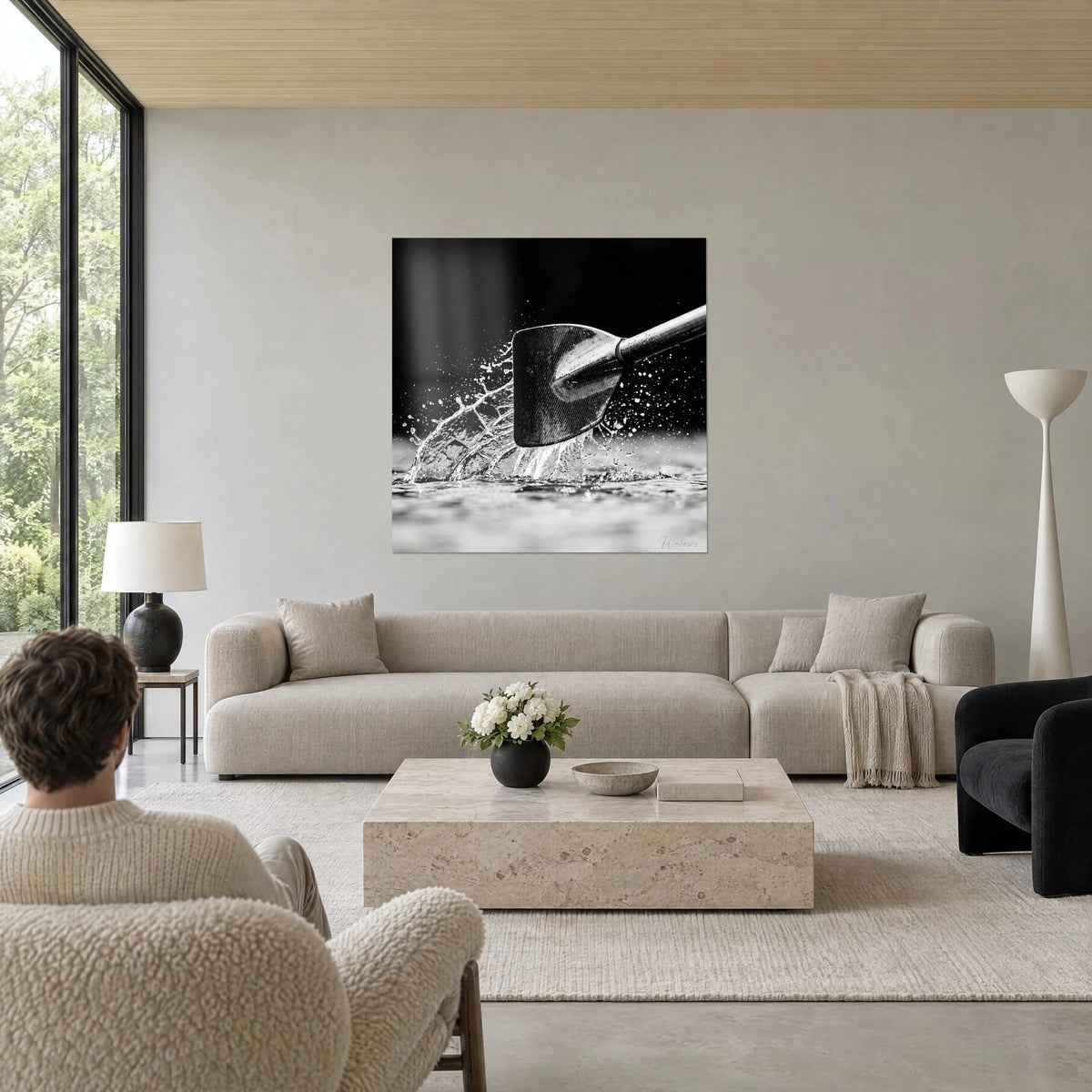 Tableau pelle de rame en carbone fendant l'eau, éclaboussures argentées sur fond noir, au-dessus d'un canapé dans un salon lumineux