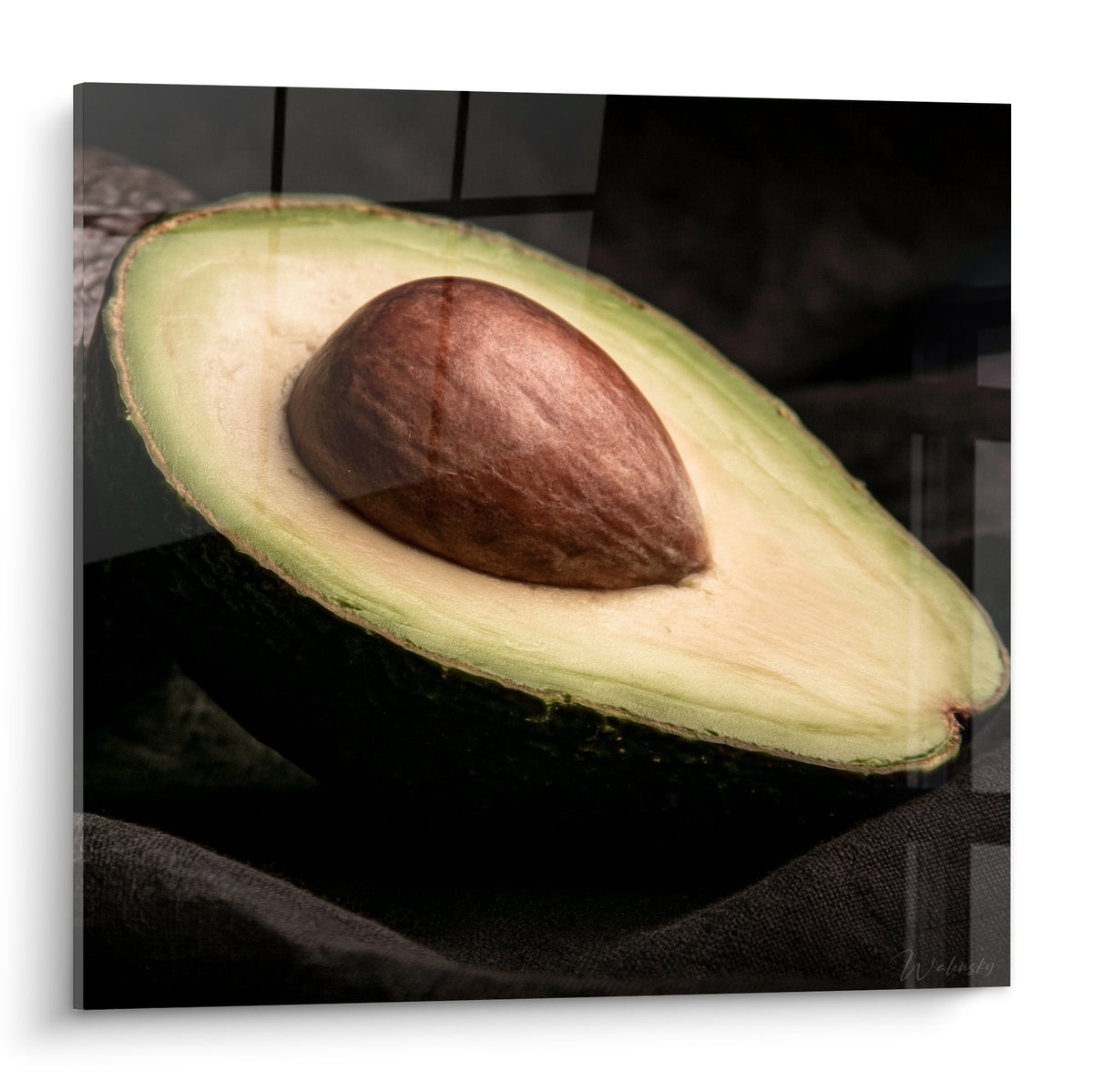 Wall art avocado cut in two, almond-green flesh and brown pit, textured anthracite background
