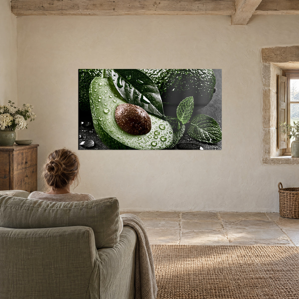 Tableau fruit rustique coupé en deux, pulpe verte et gros noyau brun humide, feuilles dentelées, face à un fauteuil en lin