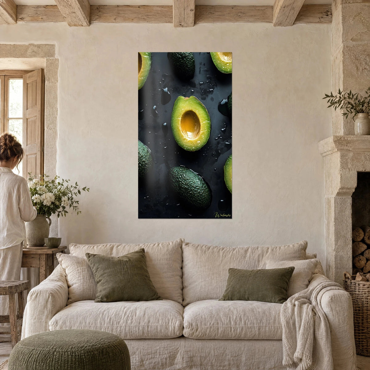 Cuadro medio aguacate verde tierno con hueso ámbar, gotas de aceite sobre fondo negro, mujer de espaldas sobre un sofá en un salón luminoso