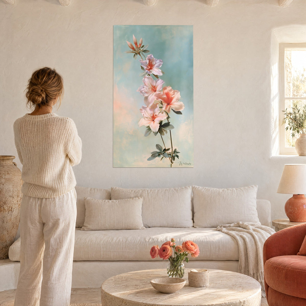 Tableau azalée rose pâle au cœur corail sur fond bleu pastel, une femme de dos devant, au-dessus d'un canapé dans un salon lumineux