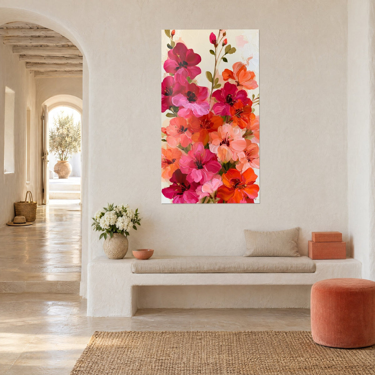 Tableau bouquet vertical de fleurs rose fuchsia et corail aux étamines dorées, fond crème, mur blanc et banquette en pierre d'une maison méditerranéenne