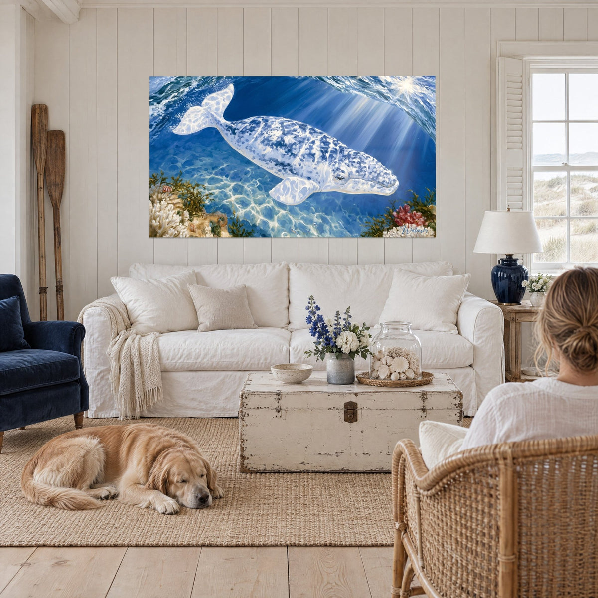Tableau baleine blanche tachetée de bleu nageant dans des rayons de soleil, récif et coraux rouges, au-dessus d'un canapé dans un salon lumineux