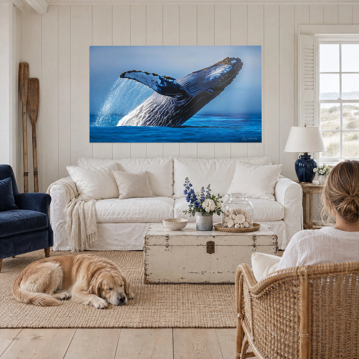 Schilderij bultrug die uit de marineblauwe golven springt met witte schuim, liggende retriever, boven een bank in een lichte woonkamer