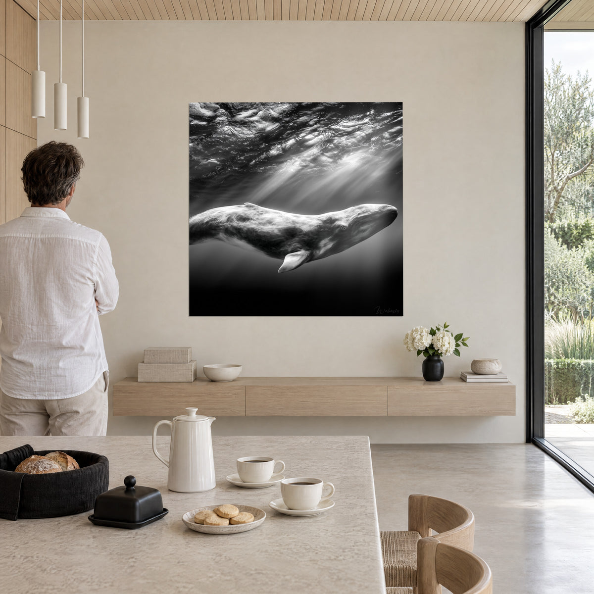 Cuadro de un mamífero marino de ojo oscuro bajo reflejos plateados de las olas, en blanco y negro, sobre una pared crema, un hombre de espaldas