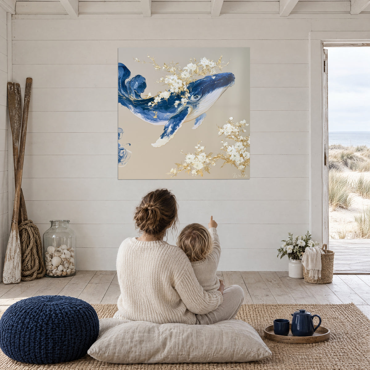 Gemälde eines ultramarinblauen Wals mit goldenen, perlmuttfarbenen Blüten vor taupefarbenem Hintergrund, betrachtet von einer Mutter und ihrem Kind am Meer