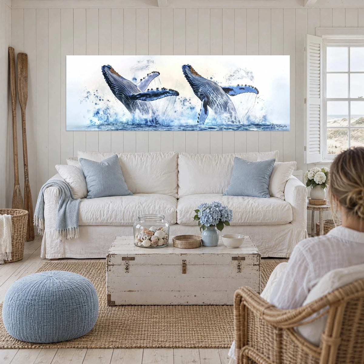 Tableau deux baleines à bosse jaillissant des flots, dos bleu nuit, nageoires blanches, écume turquoise, au-dessus d'un canapé dans un salon lumineux