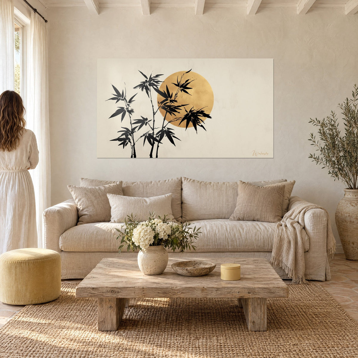 Tableau bambou noir encré devant un disque doré sur fond beige, face à une femme de dos, au-dessus d'un canapé dans un salon lumineux