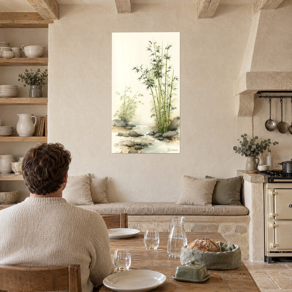 Wall art of a grove of apple green bamboo, speckled brown sand and gray pebbles, a man seen from behind seated at a table in a stone kitchen