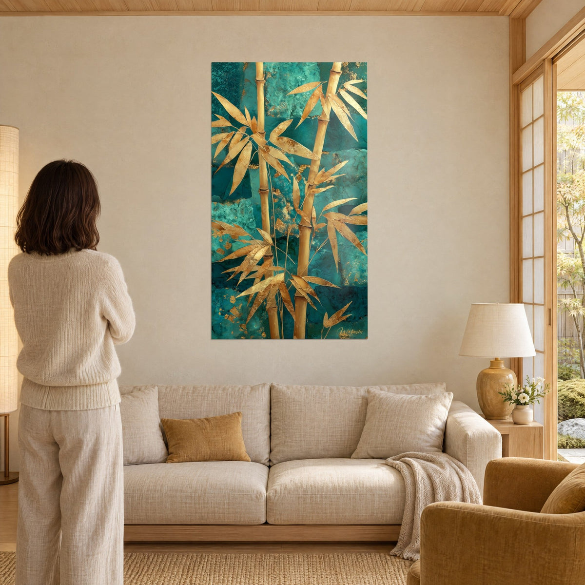 Tableau tiges de bambou dorées sur fond turquoise marbré, feuillage en or, femme de dos, au-dessus d'un canapé dans un salon lumineux