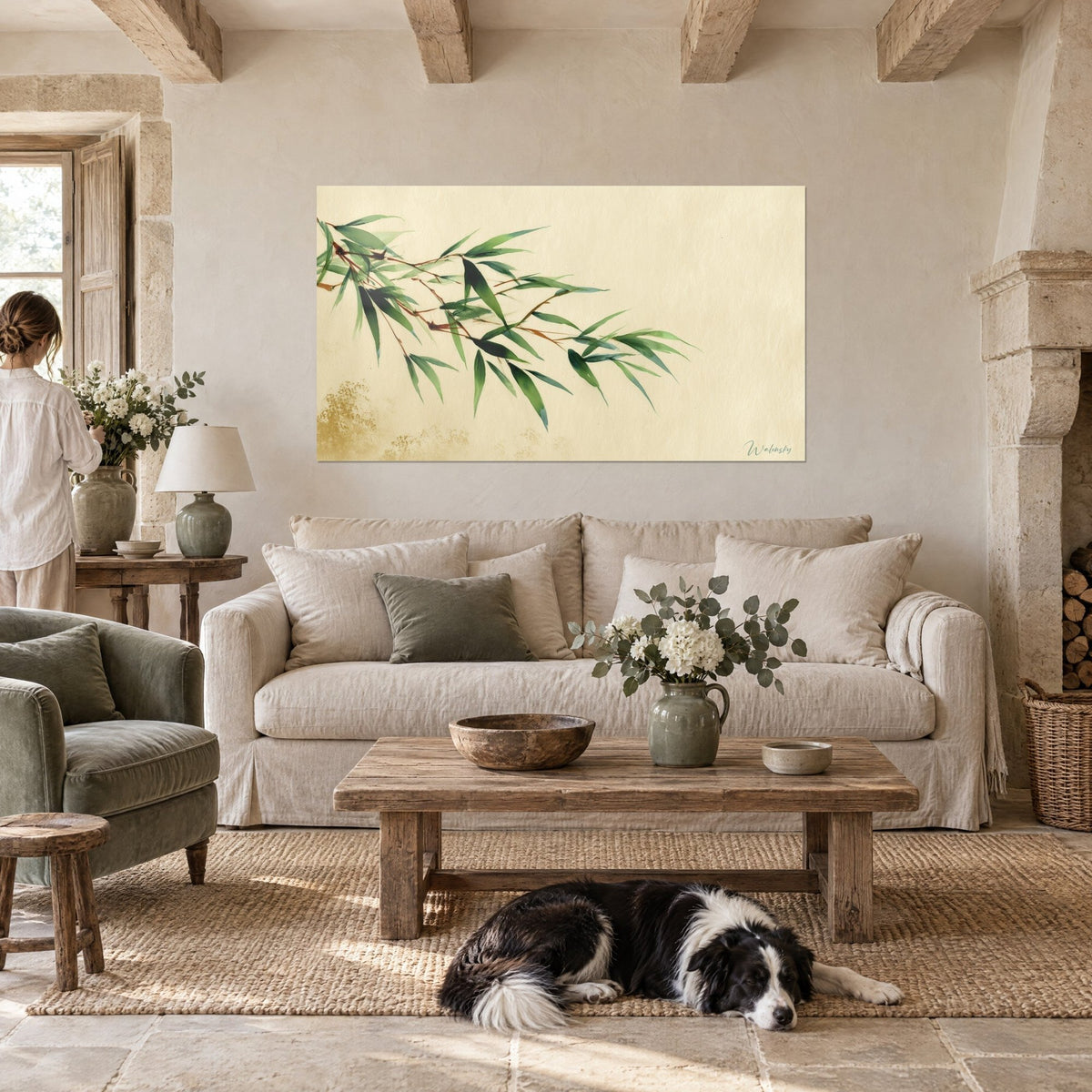 Schilderij met bamboetak, neerhangende dennengroene bladeren op beige achtergrond, liggende collie, boven een bank in een lichte woonkamer