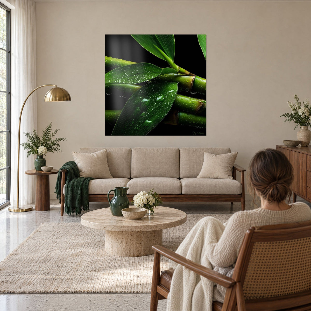 Quadro di steli di bambù verde oliva perlati di rugiada su fondo nero, donna di spalle, sopra un divano in un soggiorno luminoso
