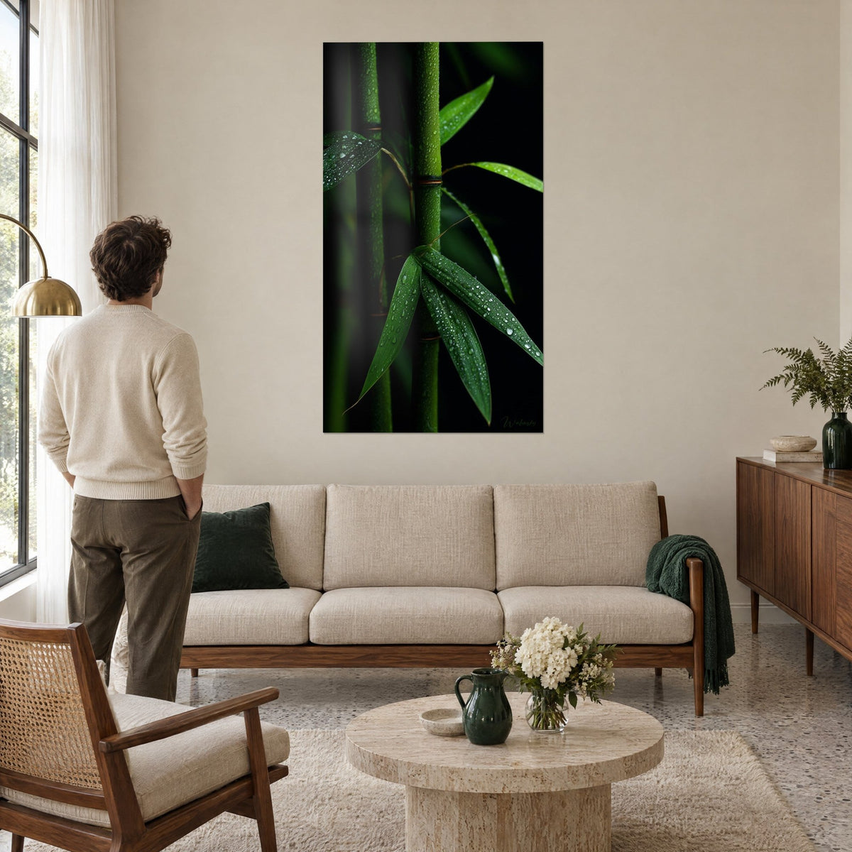 Tableau tige de bambou verte perlée de gouttes de pluie sur fond noir, homme de dos, au-dessus d'un canapé dans un salon lumineux