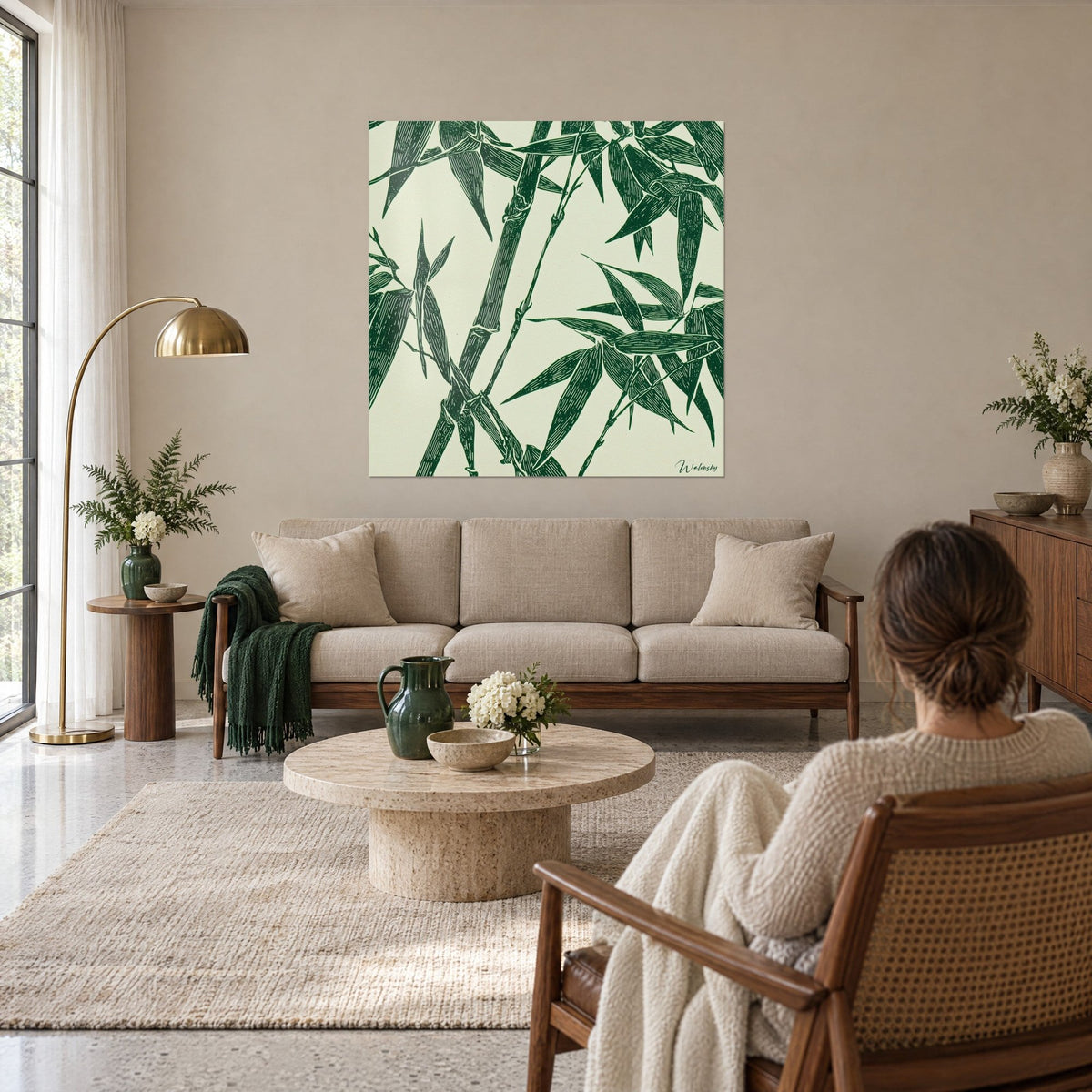 Quadro di bambù inciso in verde bosco su fondo avorio, steli incrociati e foglie lunghe, sopra un divano in un soggiorno luminoso
