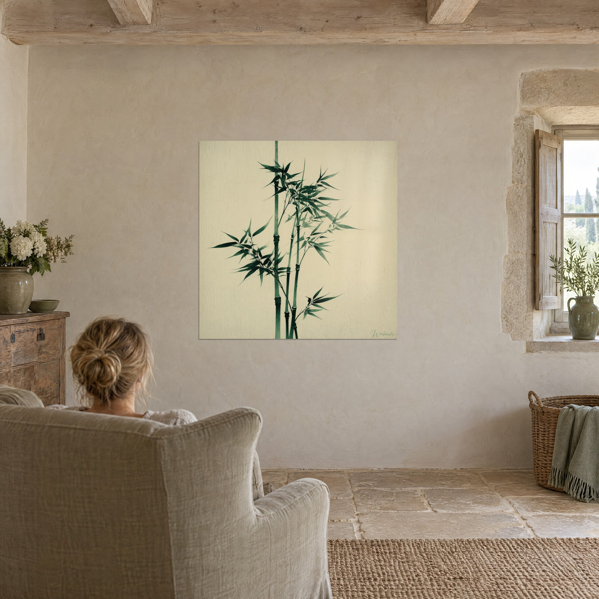 Schilderij van een bosje olijfgroene bamboestengels op een gebarsten ivoorkleurige achtergrond, een vrouw van achteren in een grijze fauteuil, stenen muur en balken