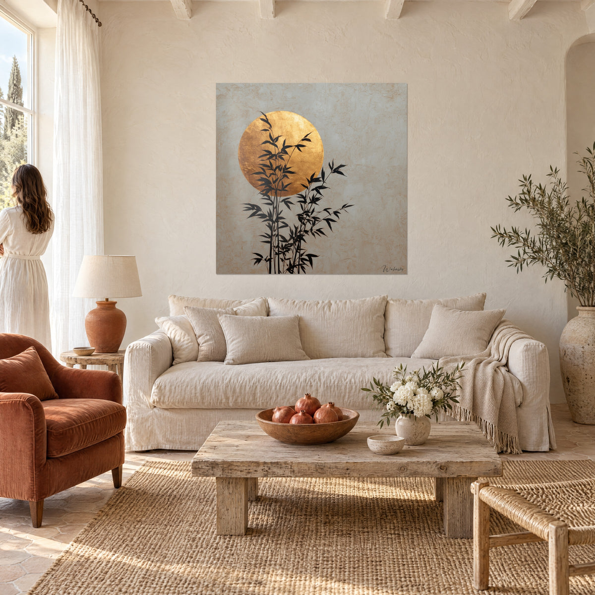 Tableau tiges de bambou noires devant un disque d'or martelé sur fond grège, au-dessus d'un canapé dans un salon lumineux
