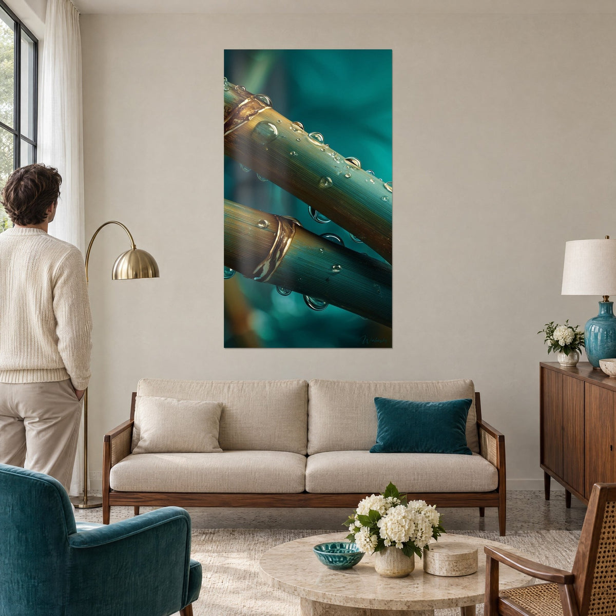 Tableau tiges de bambou dorées perlées de gouttes sur fond turquoise, couple de dos, au-dessus d'un canapé dans un salon lumineux