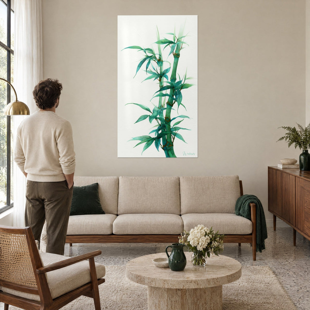 Quadro bambù acquerellato con steli slanciati verde smeraldo e nodi ocra su fondo bianco, uomo di spalle, sopra un divano in un soggiorno luminoso