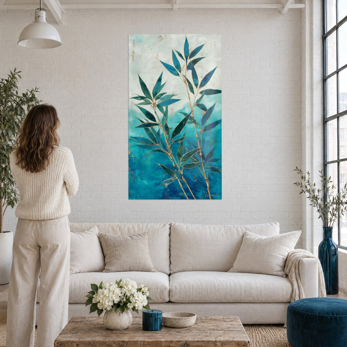 Tableau bambou aux tiges dorées sur fond turquoise et blanc crème, femme de dos, au-dessus d'un canapé dans un salon lumineux