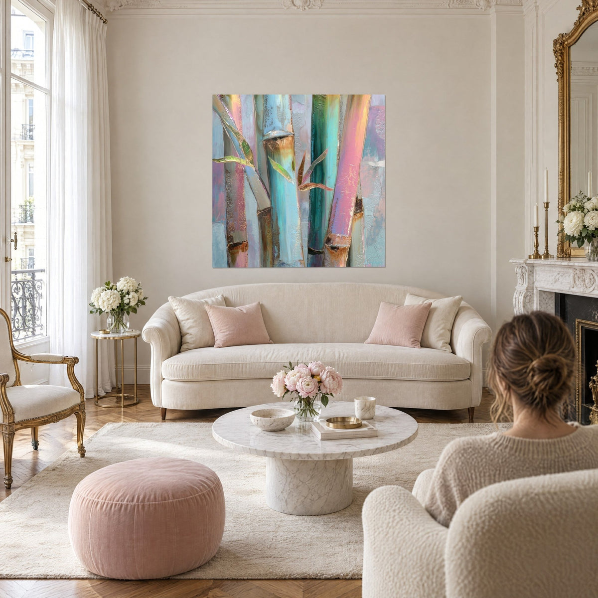 Quadro di steli di bambù turchese e rosa in pittura iridescente, foglie dorate, una donna di spalle, sopra un divano in un soggiorno luminoso