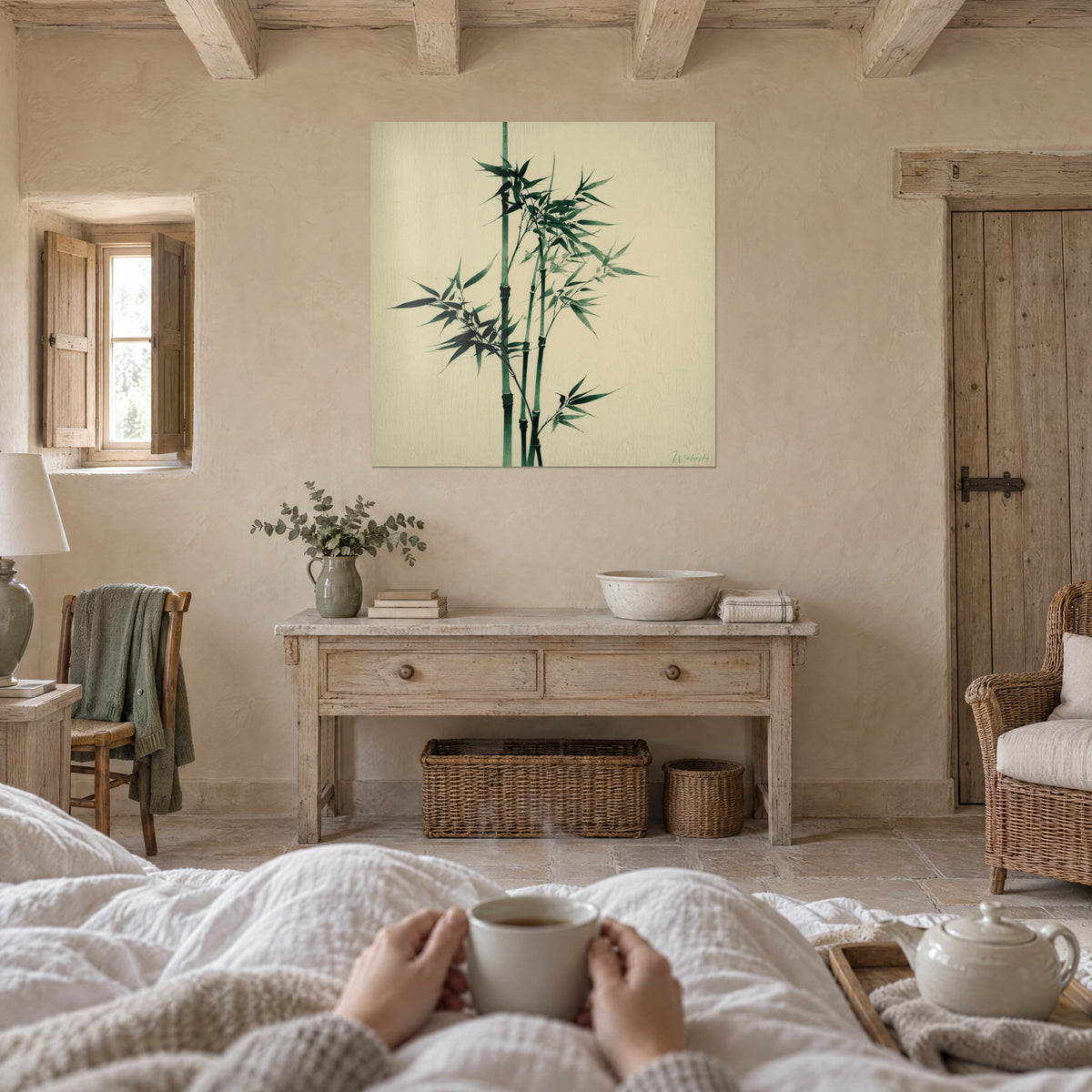 Schilderij van groene bamboestok en fijne bladeren op een gebarsten crèmekleurige achtergrond, kopje in de hand, boven een bed in een lichte slaapkamer