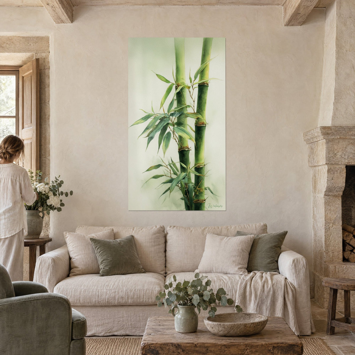 Tableau tiges de bambou vert tendre aux nœuds ocre, feuilles effilées sur fond crème, une femme de dos, au-dessus d'un canapé dans un salon lumineux