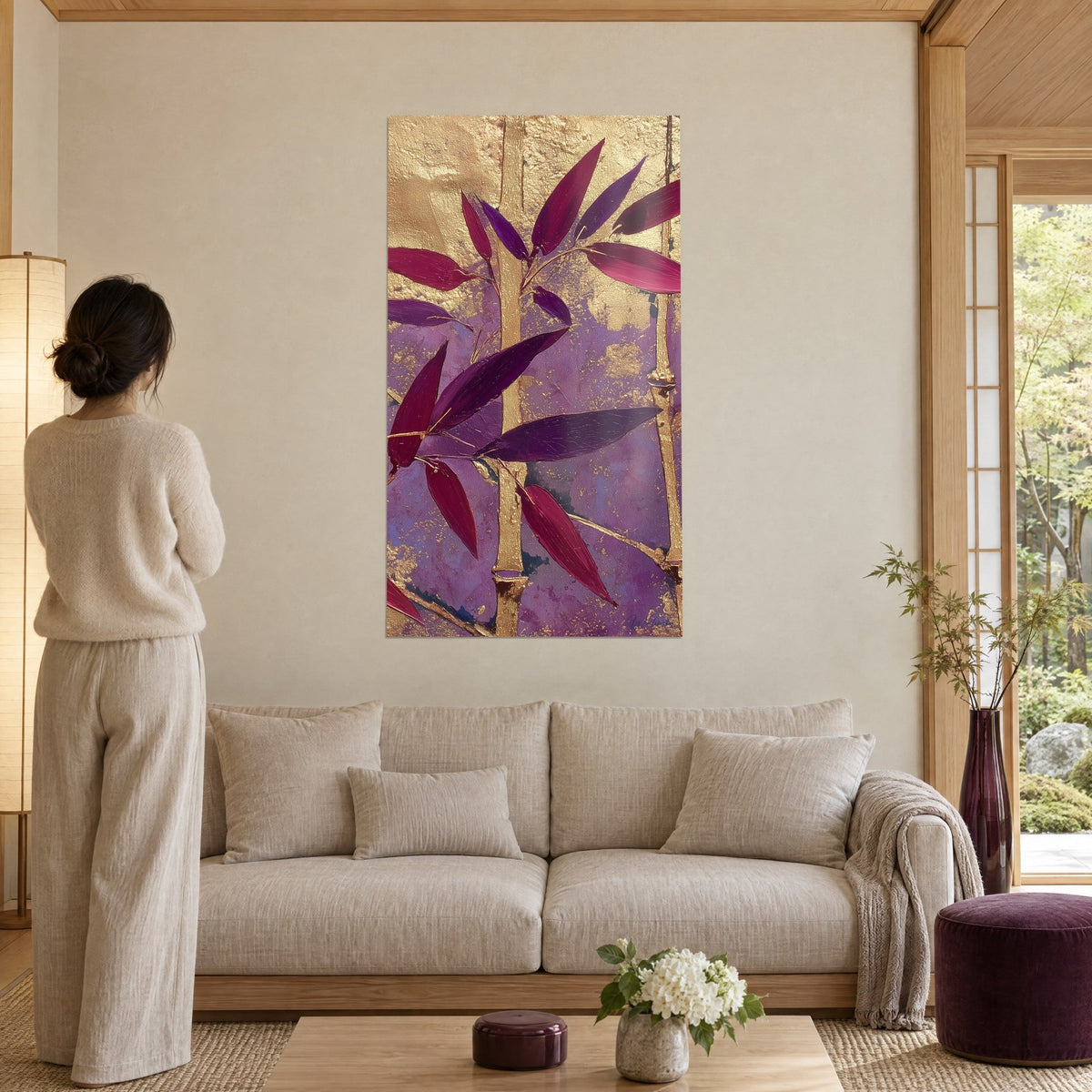 Tableau tiges de bambou dorées aux feuilles pourpres et magenta, femme de dos, au-dessus d'un canapé dans un salon lumineux