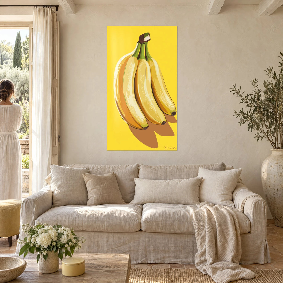 Gemälde Bananenstaude in sonnengelb, karamellbraune Schatten, eine Frau von hinten über einem Sofa in einem hellen Wohnzimmer