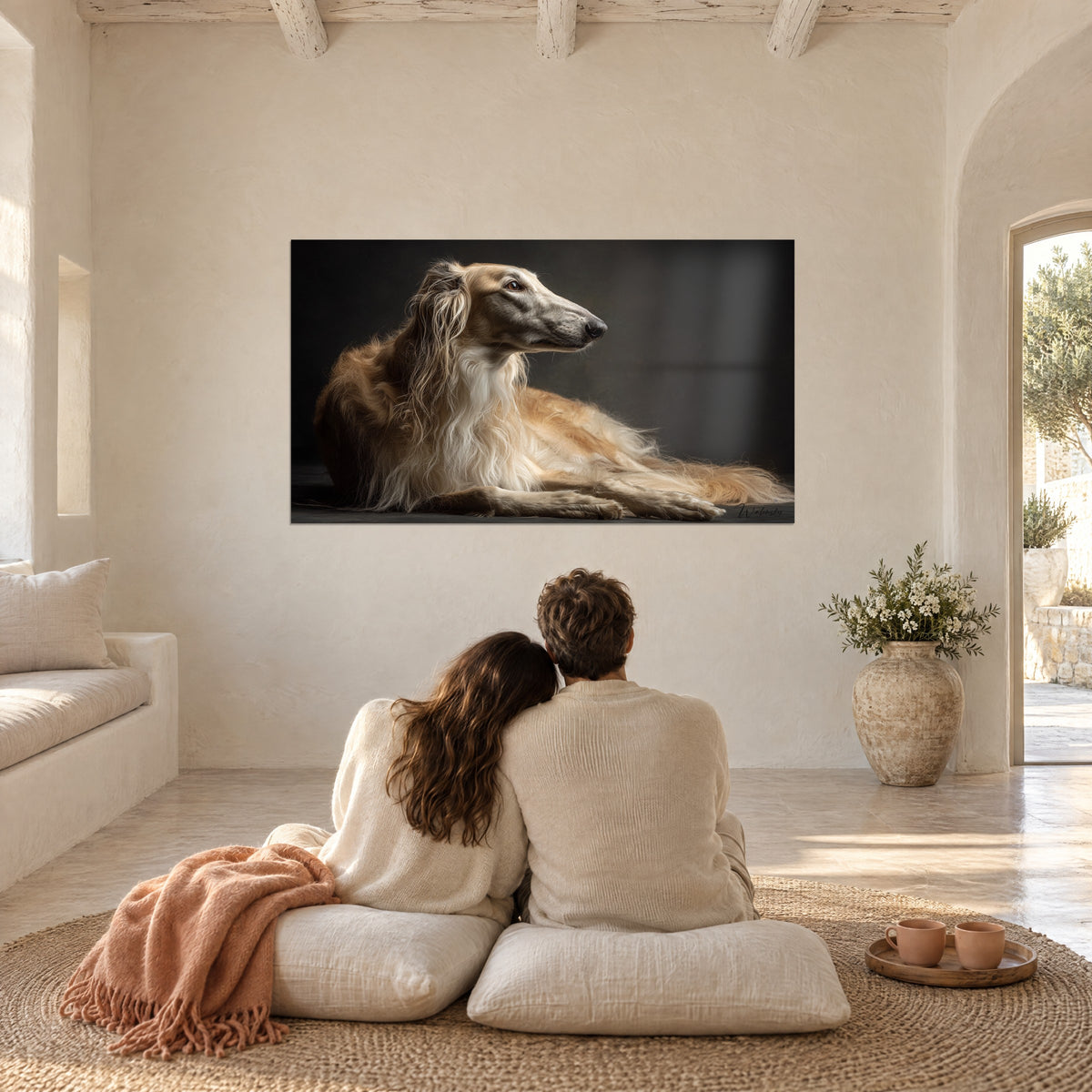 Cuadro de barzoi tumbado con flecos de pelo caramelo y crema, fondo negro profundo, frente a una pareja de espaldas sobre cojines en una habitación llena de luz