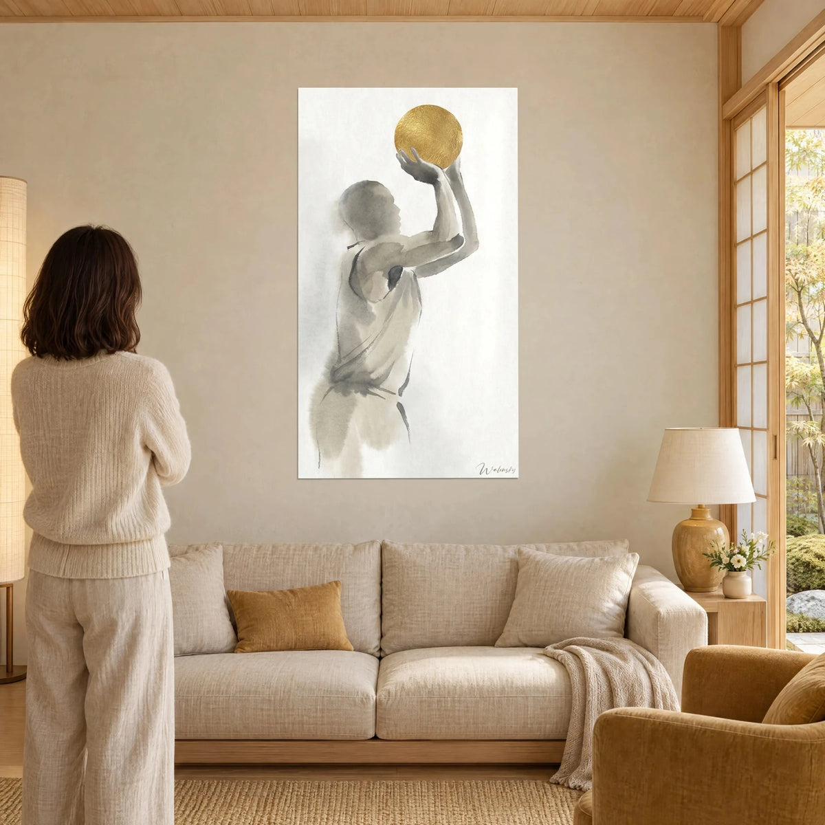 Schilderij van een basketballer in profiel, armen omhoog voor het schot, grijze inktsilhouet en gouden bal, vrouw van achteren, boven een bank in een lichte woonkamer