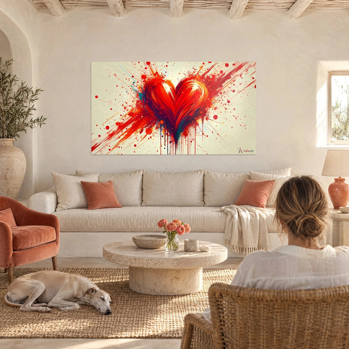Tableau cœur rouge éclaboussé de peinture orange sur fond crème, femme et lévrier endormi, au-dessus d'un canapé dans un salon lumineux