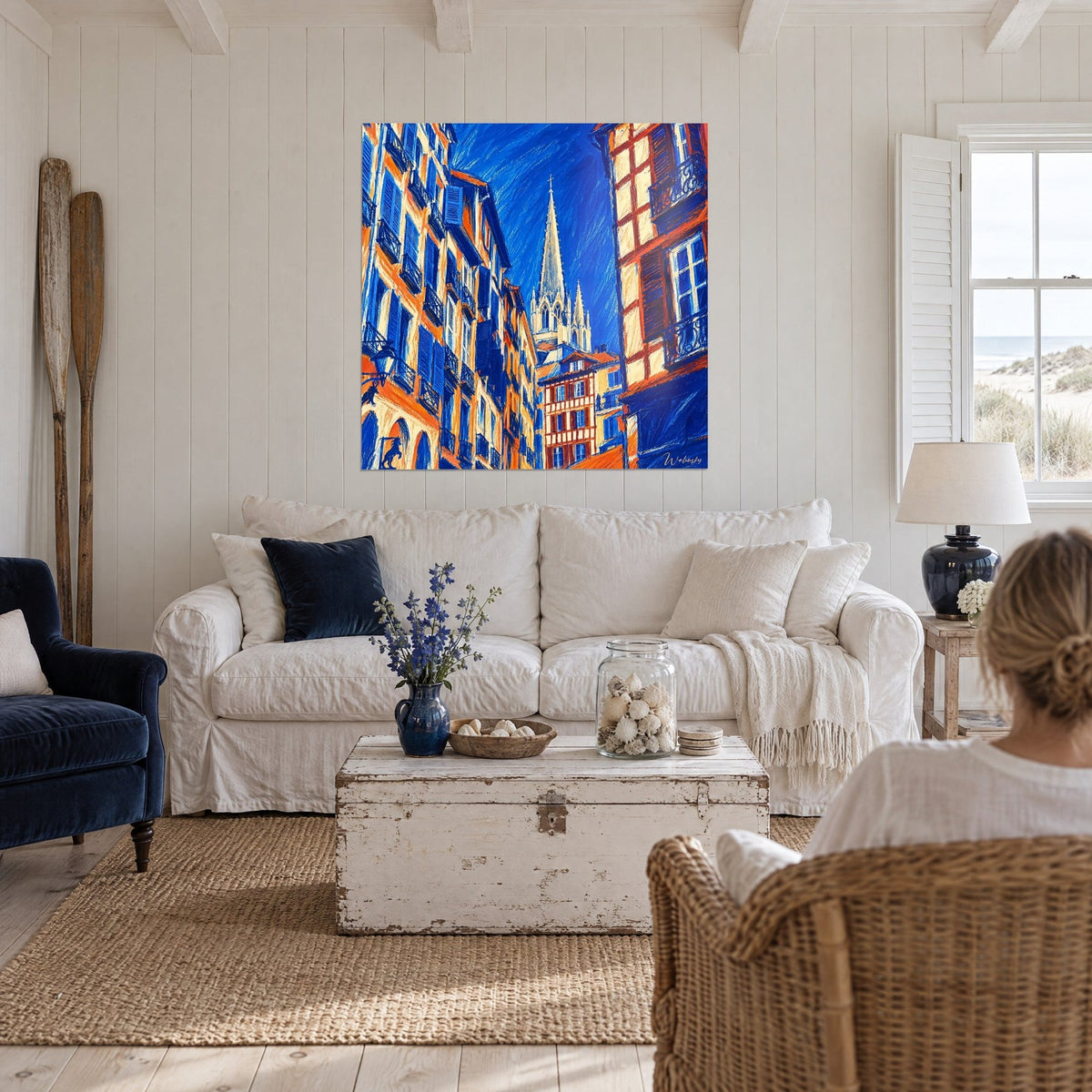 Gemälde einer gotischen Kathedrale mit hellen Spitztürmen zwischen kobaltblauen und orangefarbenen Fassaden, über einem Sofa in einem hellen Wohnzimmer