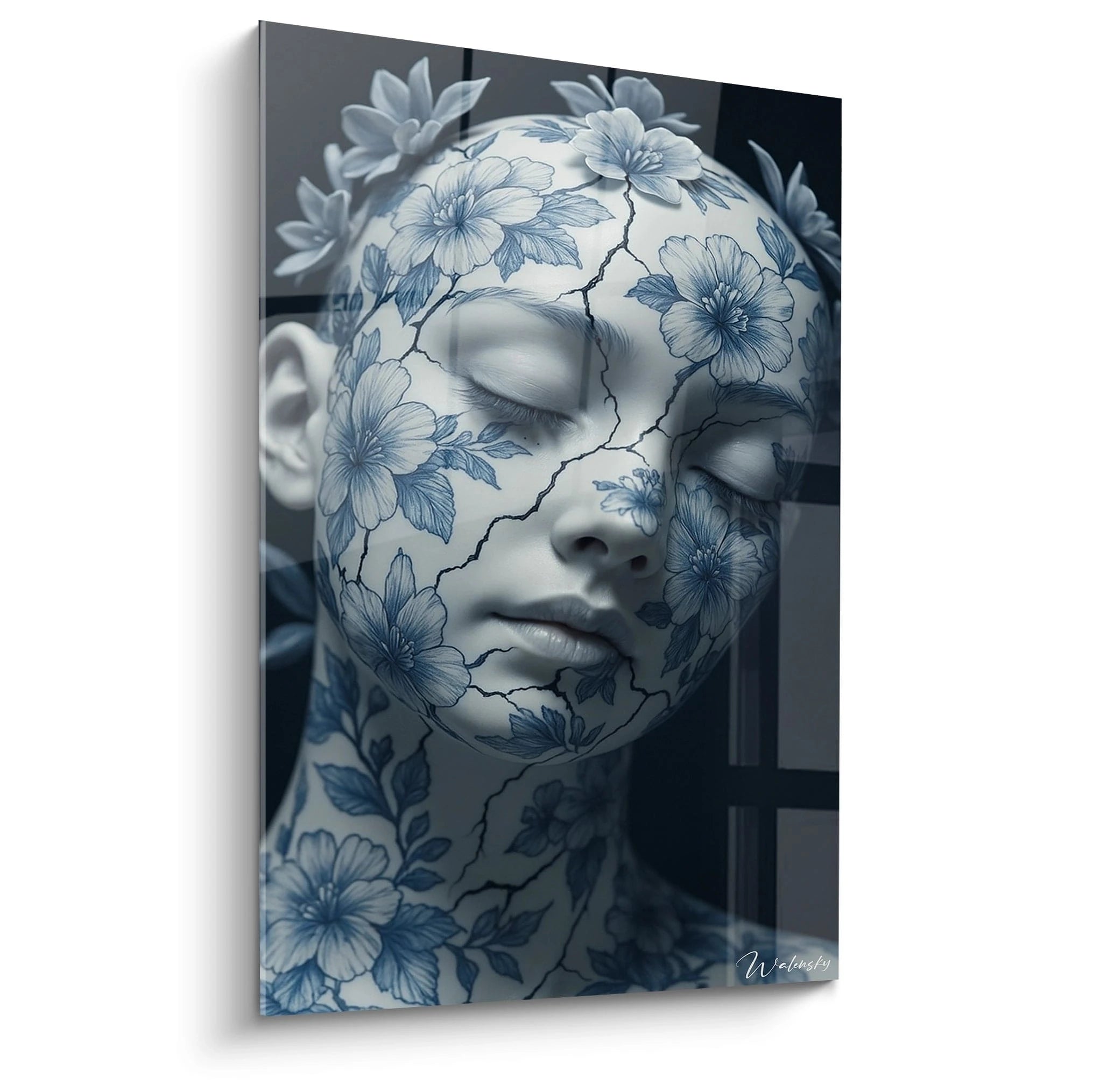 Un tableau porcelaine représentant un visage féminin aux yeux clos, orné de motifs floraux bleus sur fond blanc craquelé. Les fissures noires serpentent à travers la surface, créant un contraste saisissant avec la délicatesse des fleurs bleues et le teint blanc immaculé.
