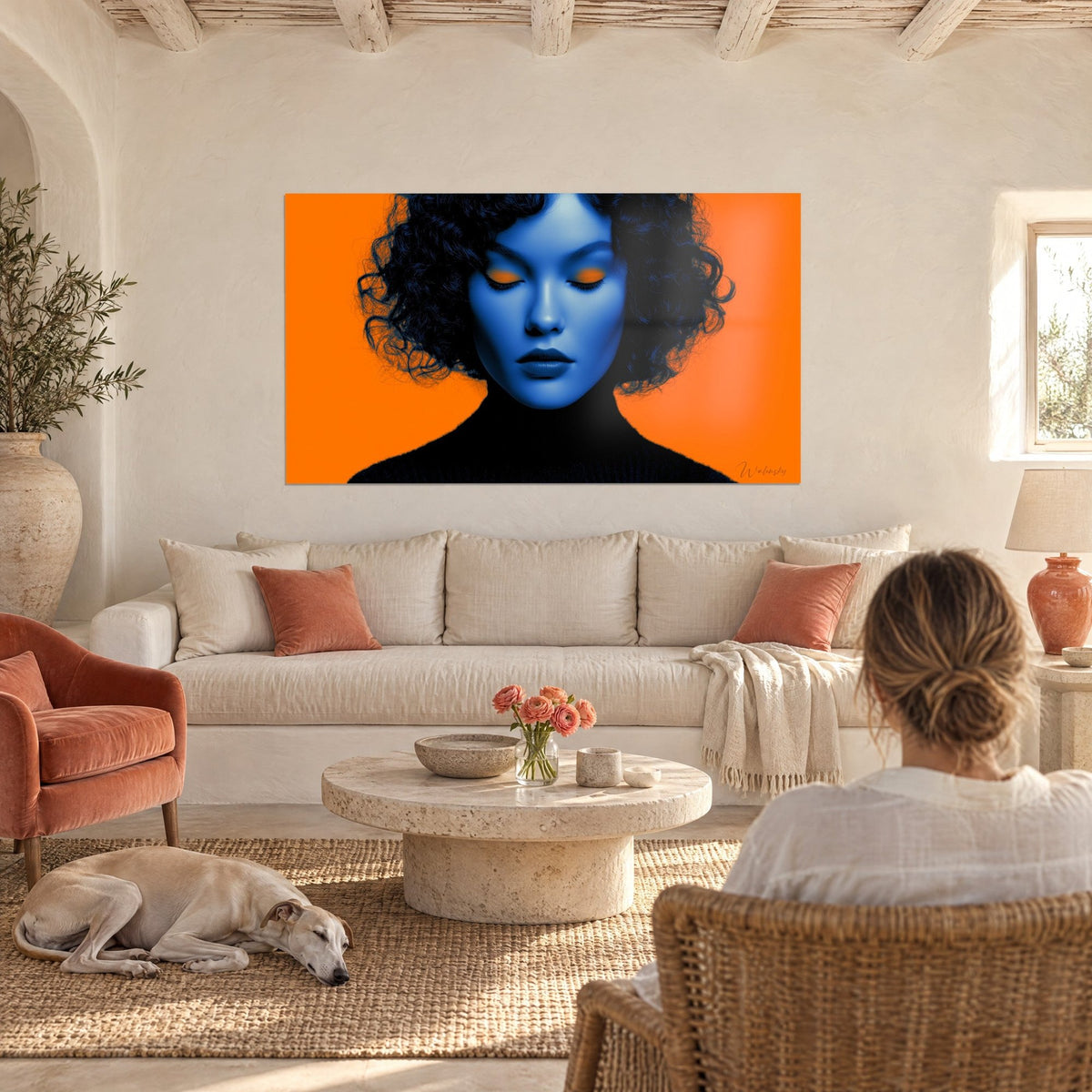 Tableau visage bleu aux paupières orange et boucles noires, fond orange vif, au-dessus d'un canapé dans un salon lumineux