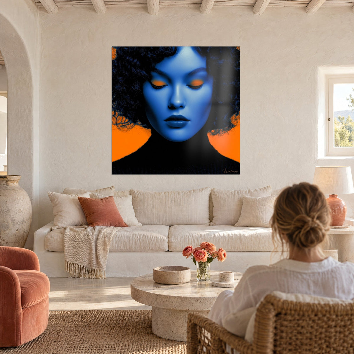 Tableau visage bleu cobalt aux paupières orange closes, cheveux bouclés noirs, au-dessus d'un canapé dans un salon lumineux
