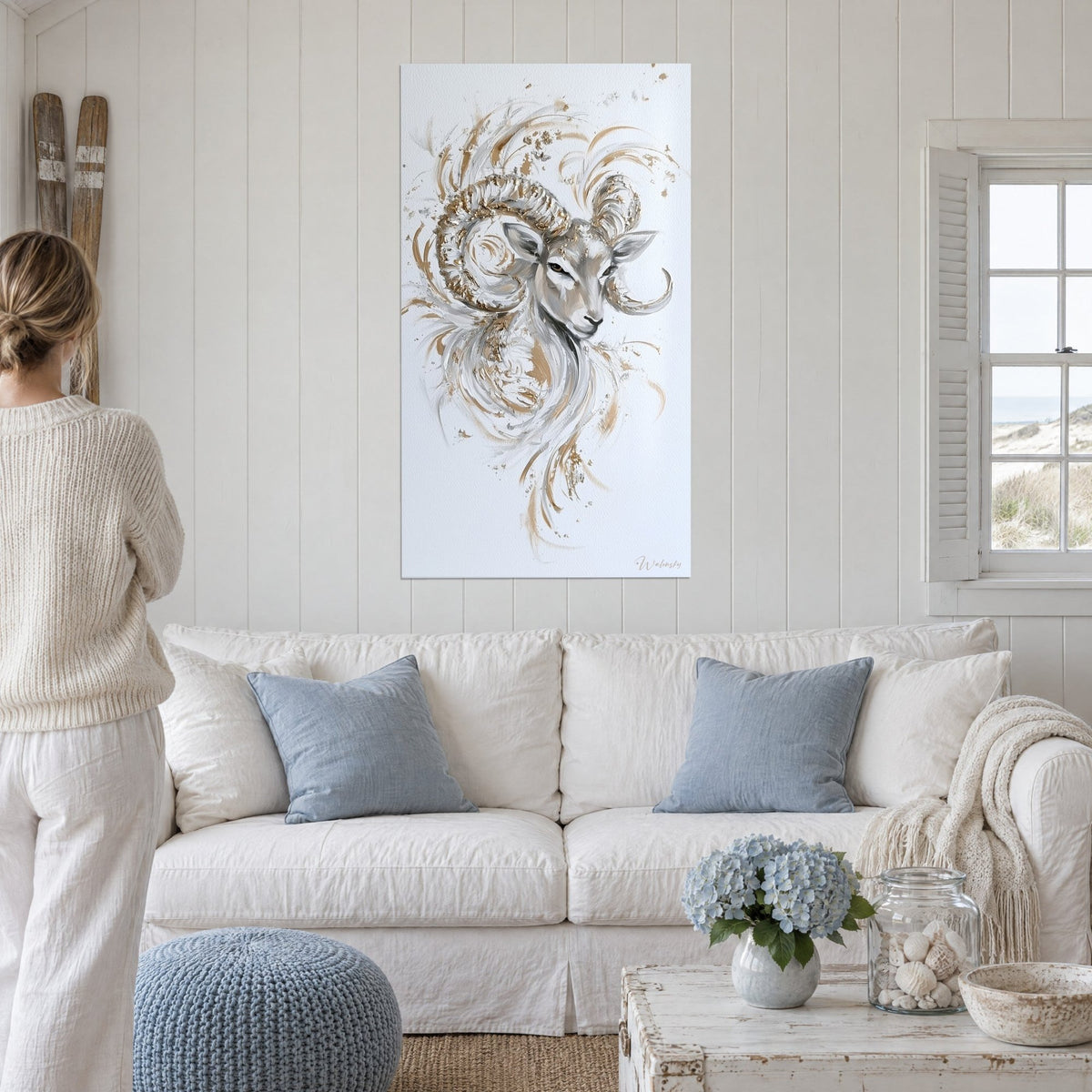 Quadro ariete con corna a spirale dorate, pelo grigio perla, persona di spalle, sopra un divano in un soggiorno luminoso