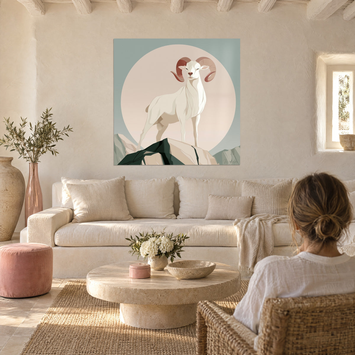 Quadro montone avorio dalle corna terracotta davanti a un disco rosa cipria, donna di spalle, sopra un divano in un soggiorno luminoso