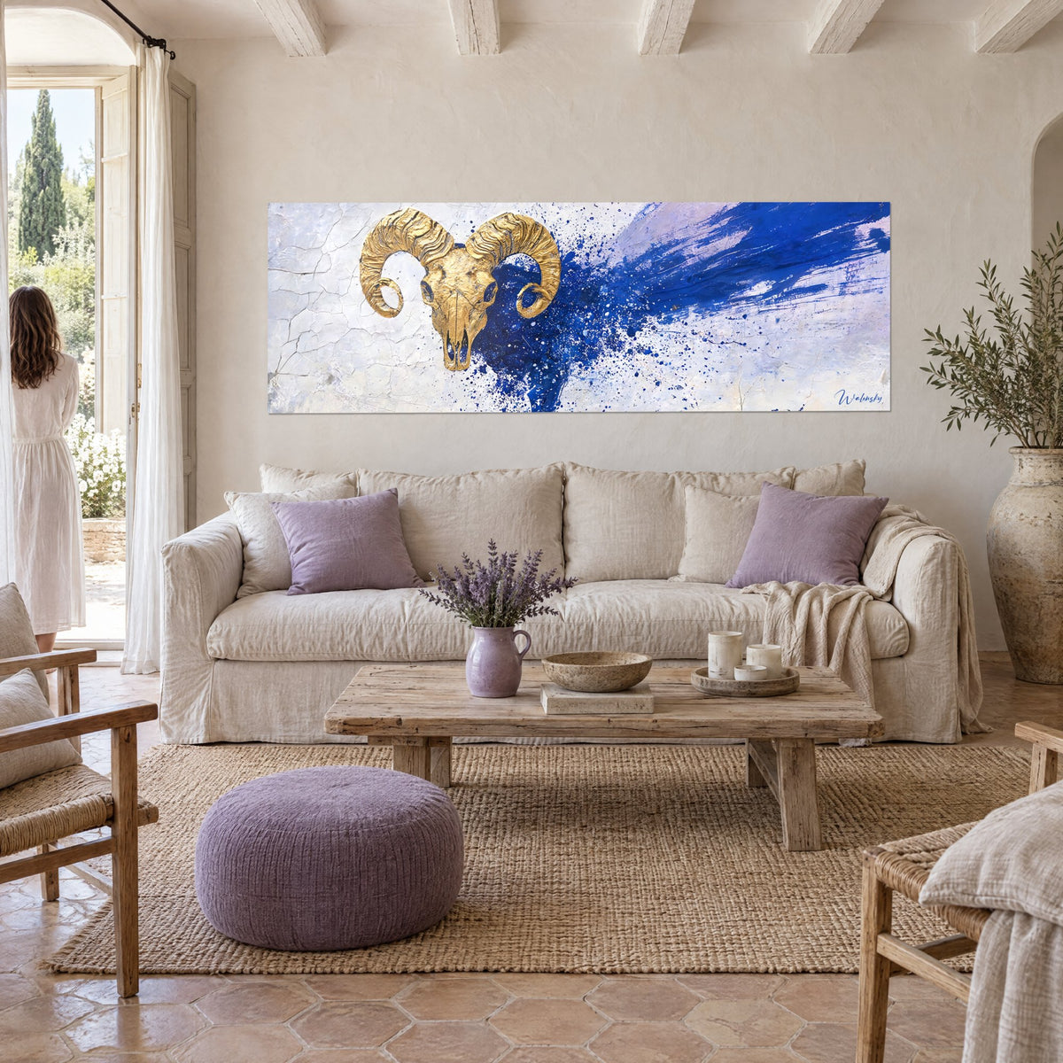 Tableau crâne de bélier en or aux cornes spiralées, éclaboussures bleu marine sur fond blanc craquelé, au-dessus d'un canapé dans un salon lumineux