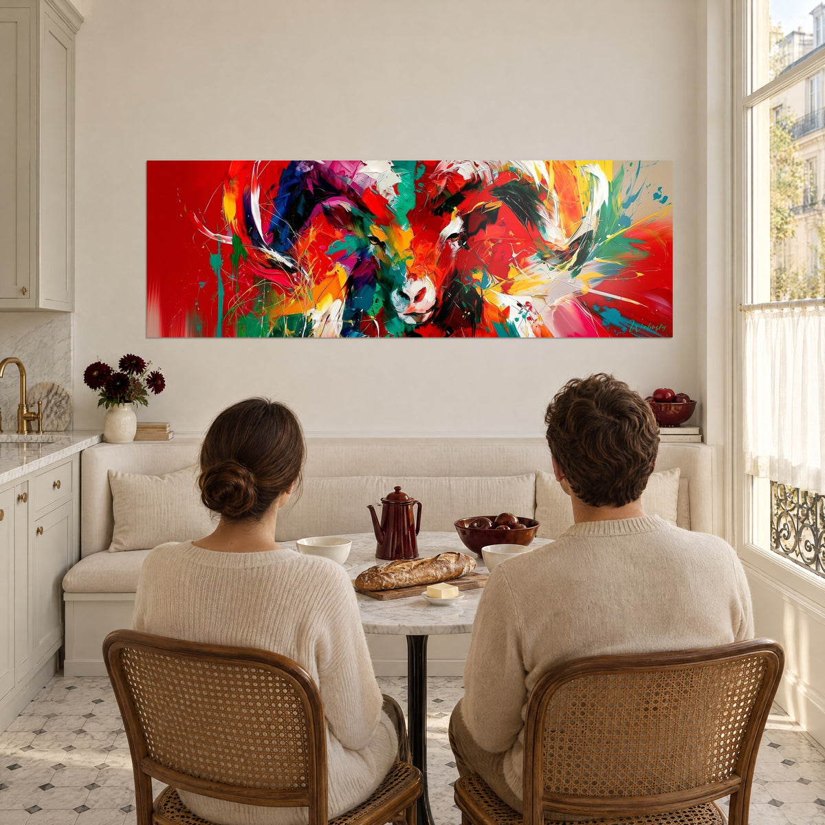 Tableau charge fulgurante d'un bélier peint en rouge, jaune et turquoise, que deux convives de dos admirent depuis la cuisine ouverte