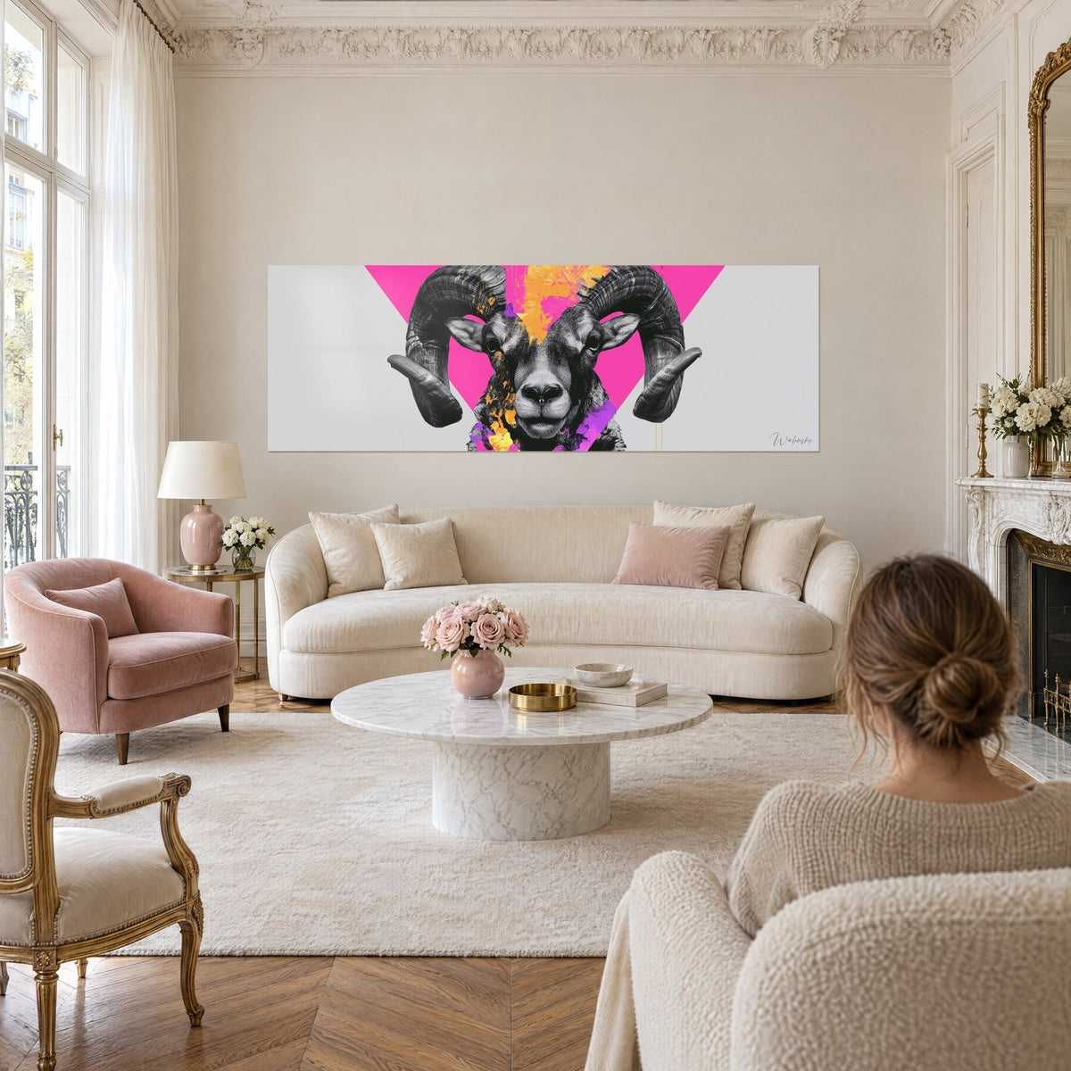 Quadro ariete dalle corna nere a spirale, triangolo fucsia e schizzi gialli, due persone di spalle, sopra un divano in un soggiorno luminoso