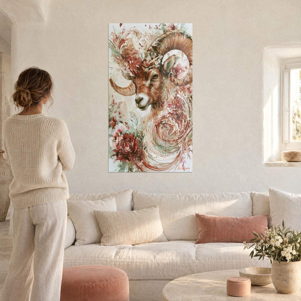 Tableau bélier aux cornes spiralées, pelage fauve et roses vert sauge, une femme de dos au-dessus d'un canapé dans un salon lumineux